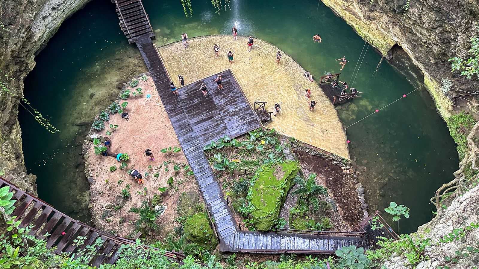 Vue plongeante sur un cénote ouvert, avec ses passerelles en bois et ses baigneurs, près de Cancún