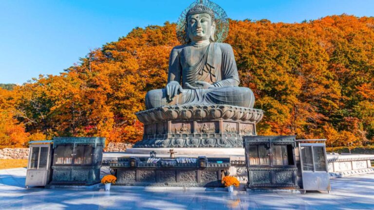 Un grand bouddha de bronze au temple Naksansa, entouré de forêt aux couleurs d'automne