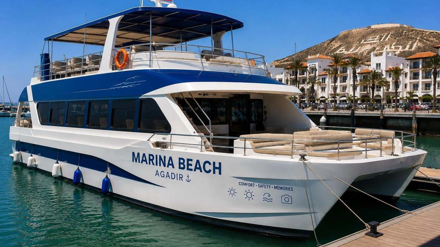 Un bateau d'excursion amarre dans le port d'Agadir, avec la colline et son inscription en arriere-plan