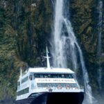 Un bateau de croisière passe devant une cascade de Milford Sound, encaissée entre les parois du fjord